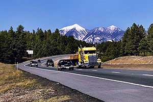 cars and yellow Semi Truck leaving Flagstaff and San Francisco Peaks behind
