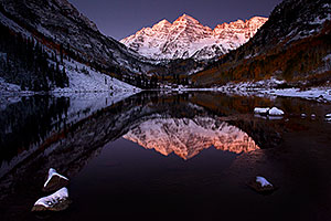 Snowy reflection of Maroon Bells with an icy cover along the shore
